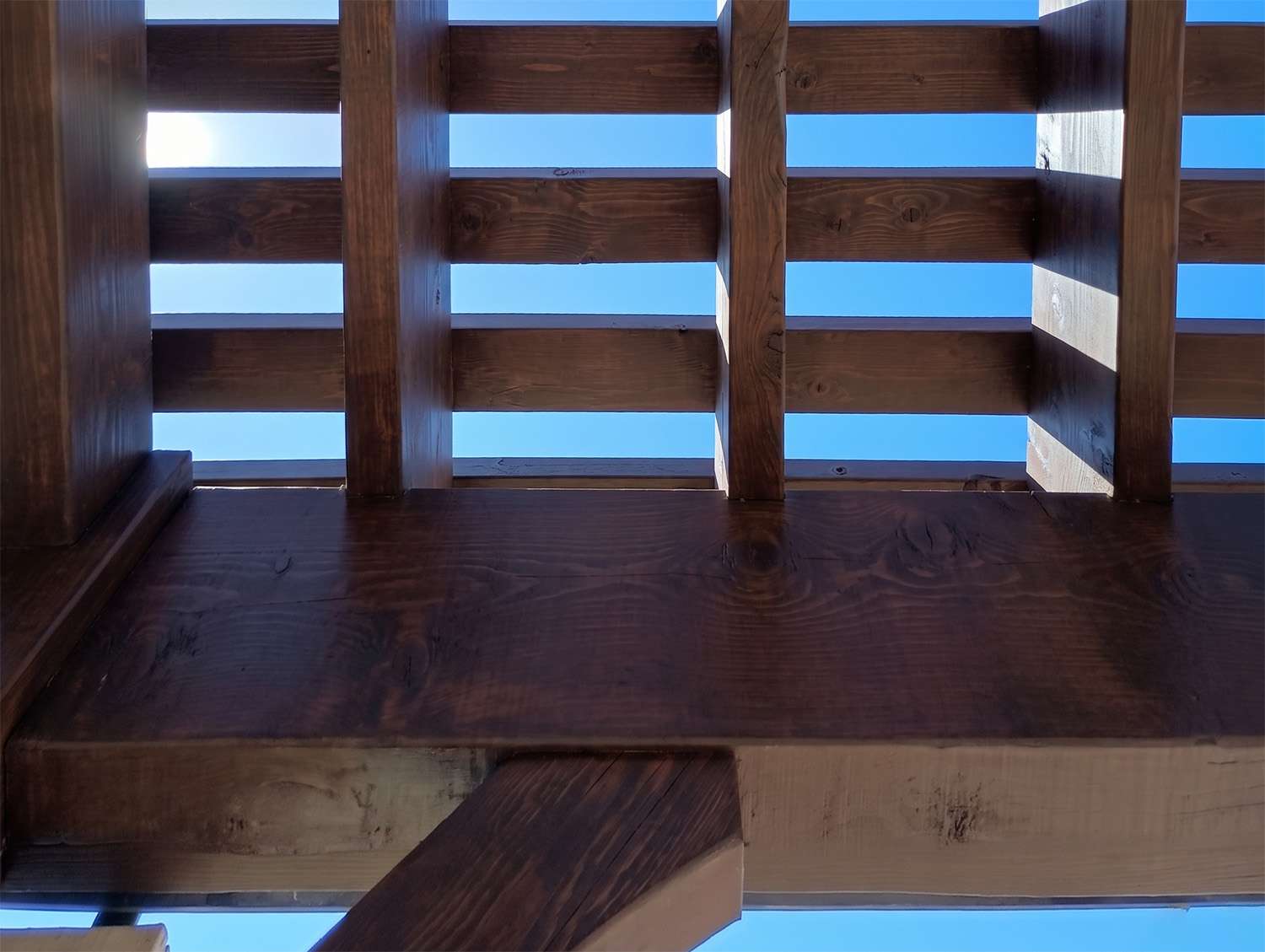 Close-up view looking upward through a Western Timber Frame pergola, showing thick timber rafters and shade planks designed to create deep shade coverage and outdoor comfort.